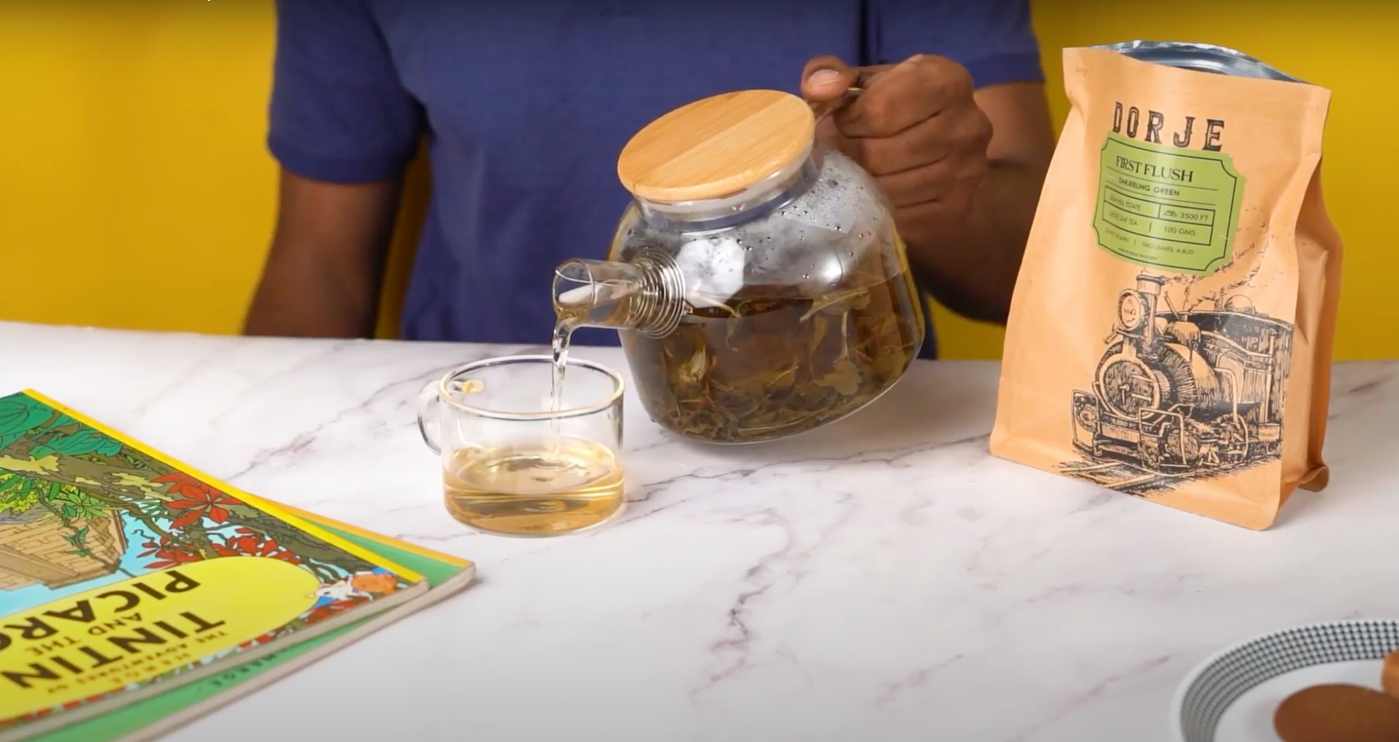 Green Darjeeling Tea Being poured into a glass cup with a tintin book kept near it