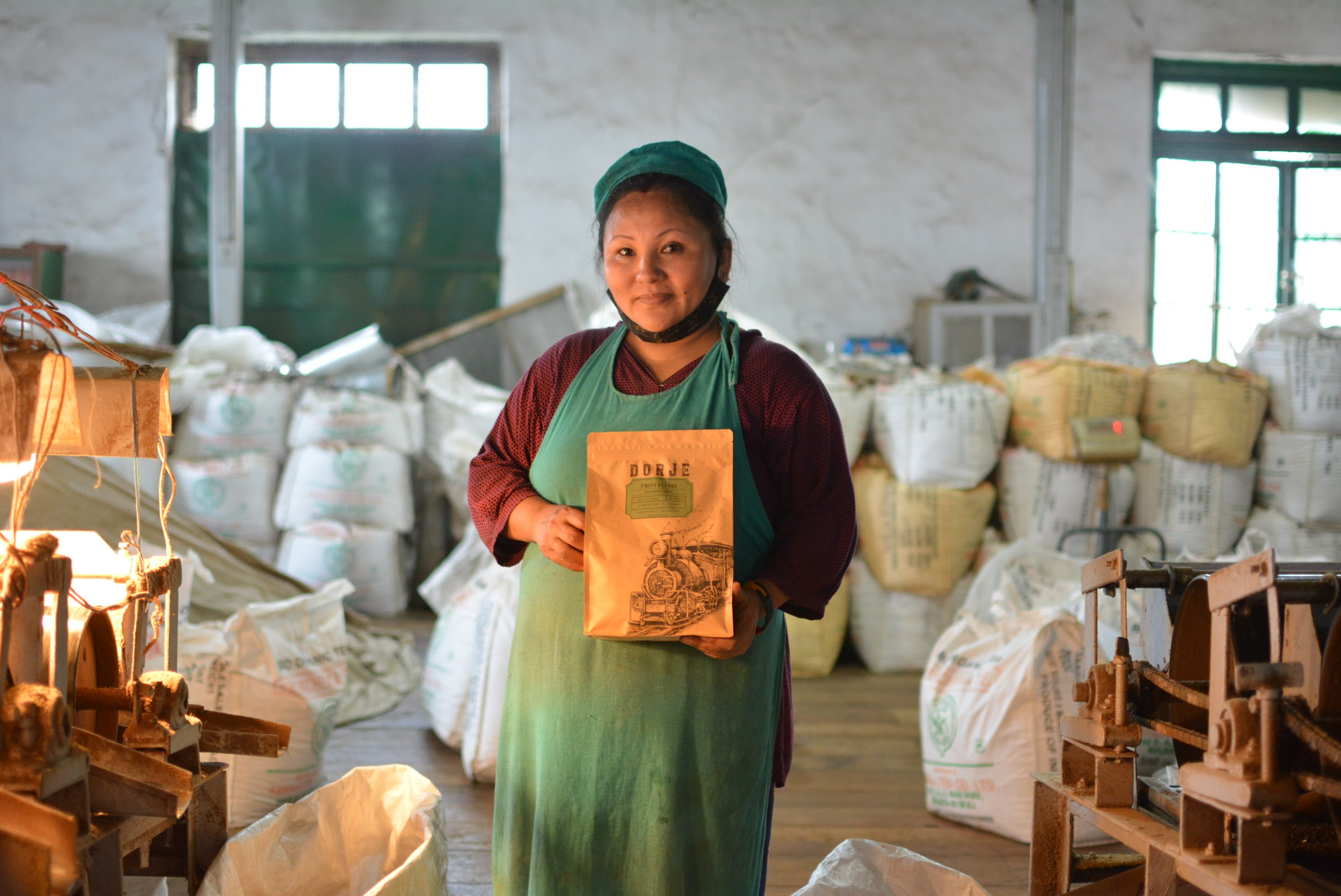 A Woman in factory overalls holding a packet of Darjeeling Tea